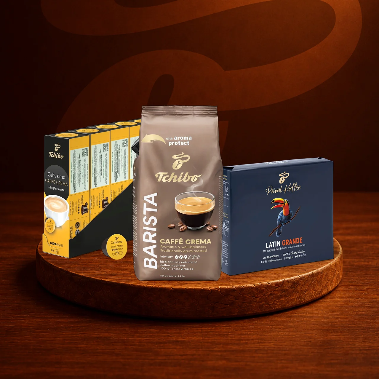 Ahşap bir stand üzerinde üç Tchibo kahve ürünü: solda Cafissimo Caffè Crema kapsül paketi, ortada Barista Caffè Crema öğütülmüş kahve paketi ve sağda Privat Kaffee Latin Grande paketi.