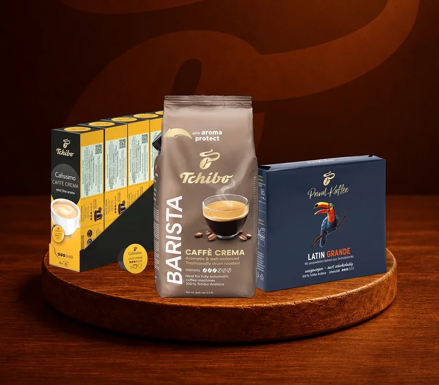 Ahşap bir stand üzerinde üç Tchibo kahve ürünü: solda Cafissimo Caffè Crema kapsül paketi, ortada Barista Caffè Crema öğütülmüş kahve paketi ve sağda Privat Kaffee Latin Grande paketi.