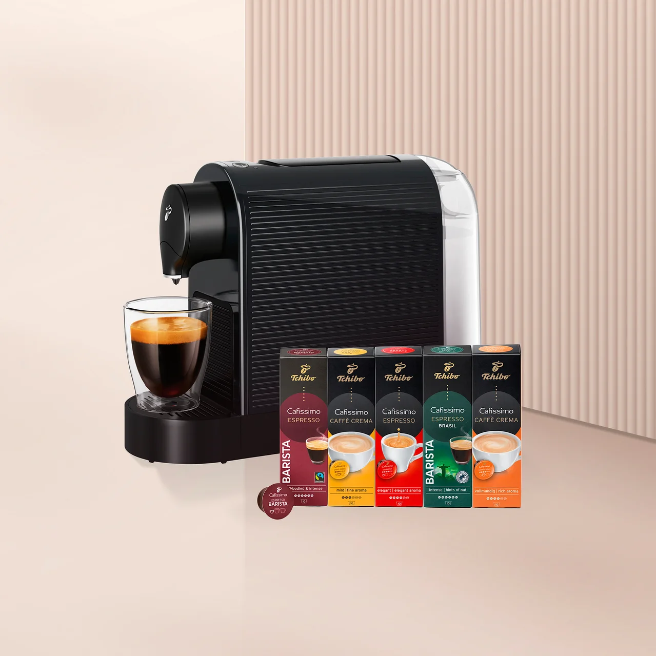 Siyah beyaz kapsül kahve makinesi, altında cam bir fincan kahve ve yanında beş kutu Tchibo Cafissimo kahve kapsülü ile bir adet Barista kapsülü.