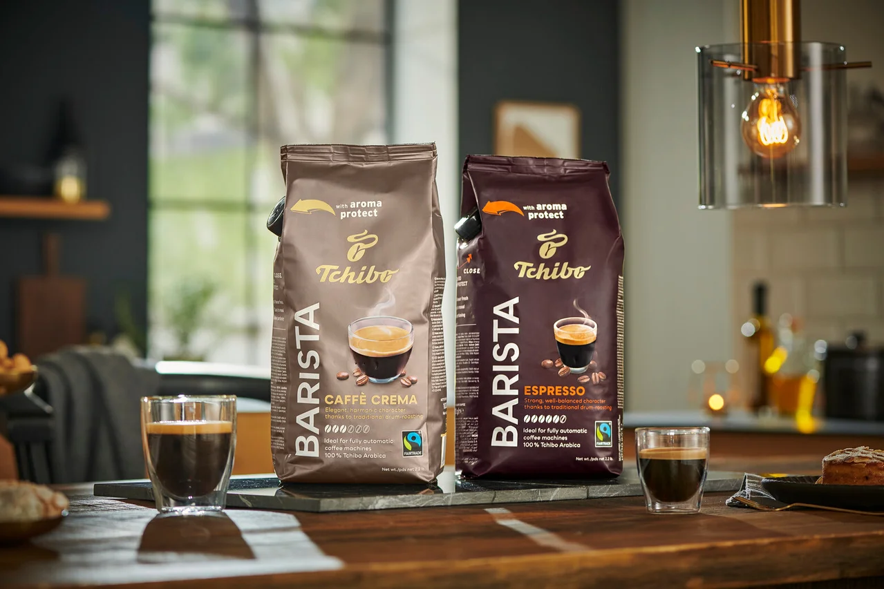 İki paket Tchibo Barista kahve, bir Caffe Crema ve bir Espresso, ahşap bir masa üzerinde yan yana duruyor.