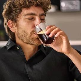 Adam çift cidarlı bardaktan kahve içiyor.