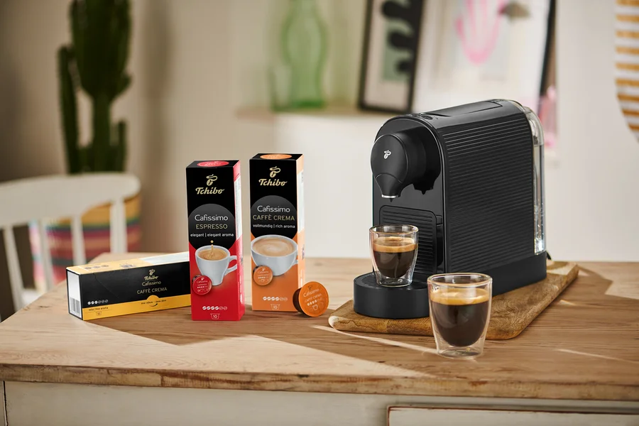 Siyah bir Cafissimo pure+ kahve makinesi, yanında iki bardak kahve ile birlikte ahşap bir tahta üzerinde duruyor.