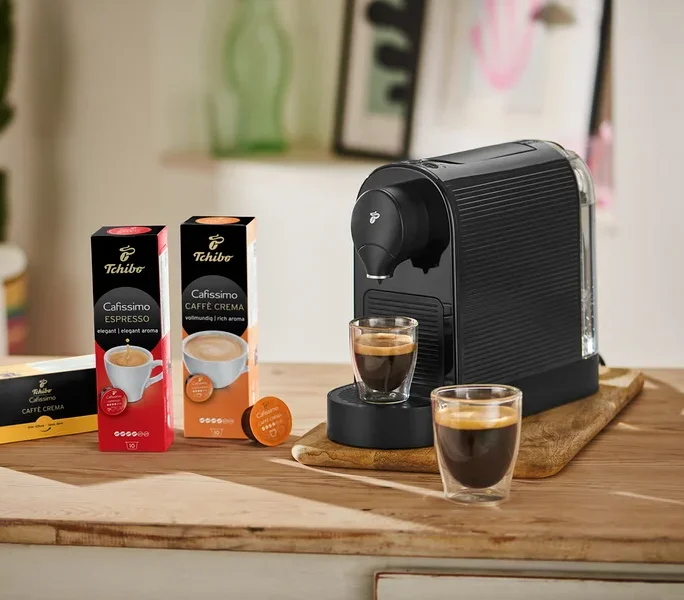 Siyah bir Cafissimo pure+ kahve makinesi, yanında iki bardak kahve ile birlikte ahşap bir tahta üzerinde duruyor.