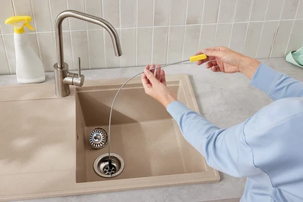 Bir kişi, mutfak lavabosu giderini temizlemek için bir lavabo açma teli kullanıyor.