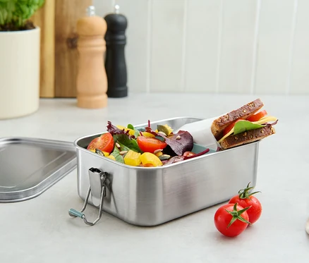 Paslanmaz çelik yemek kutusunda salata ve sandviç, yanında iki domates duruyor.
