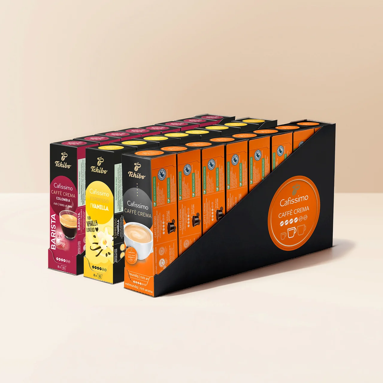 Siyah bir teşhir standında birden fazla sıra Tchibo Cafissimo kahve kapsülü kutusu bulunuyor. Görünen çeşitler arasında pembe Caffè Crema Colombia, sarı Espresso Vanilla ve turuncu Caffè Crema kutuları yer alıyor. Standın yanında turuncu bir Cafissimo logosu var.
