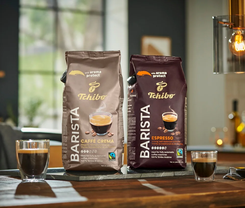 İki paket Tchibo Barista kahve, bir Caffe Crema ve bir Espresso, ahşap bir masa üzerinde yan yana duruyor.
