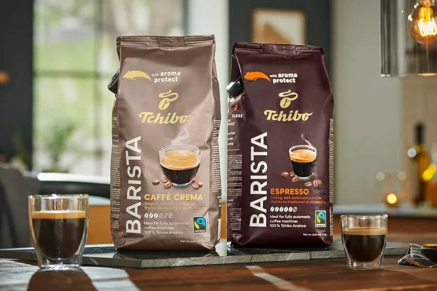 İki paket Tchibo Barista kahve, bir Caffe Crema ve bir Espresso, ahşap bir masa üzerinde yan yana duruyor.
