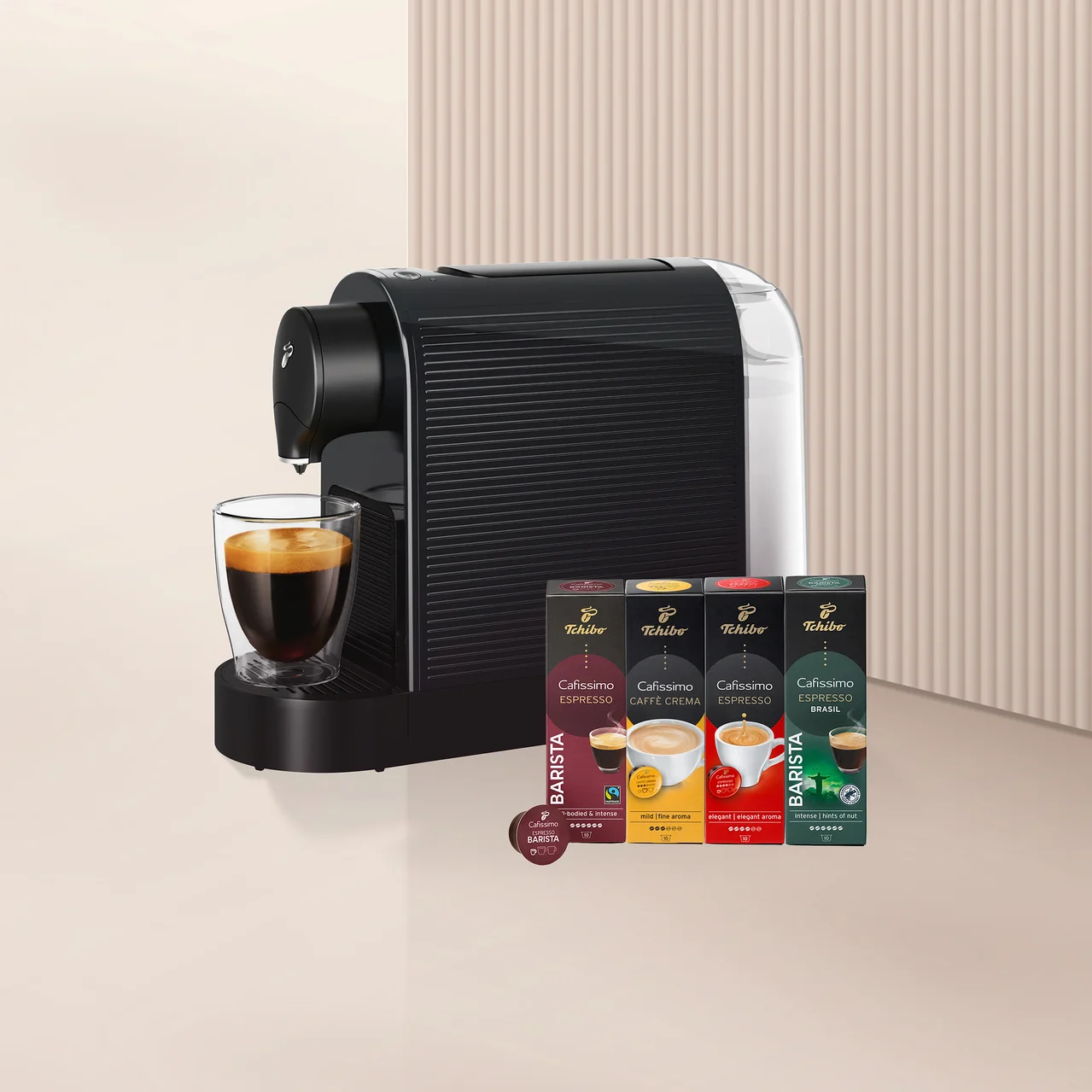 Siyah beyaz bir Tchibo Cafissimo kahve makinesi, şeffaf bir cam bardağa espresso dolduruyor. Yanında dört kutu Tchibo Cafissimo Barista Edition kapsülü (Espresso, Caffè Crema, Espresso, Espresso Brasil) ve bir adet tek kapsül bulunuyor.