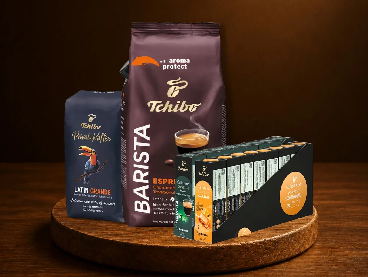 Ahşap tepside üç Tchibo kahve ürünü. Solda "Privat Kaffee Latin Grande" çekirdek kahve, arkada "Barista Espresso" çekirdek kahve, sağda "Cafissimo Espresso Caramel" kapsülleri.