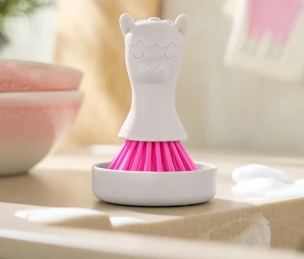 Pembe kıllı beyaz lama şeklindeki fırça, sabun kalıntılarının olduğu lavabonun üzerinde beyaz bir kapta duruyor.