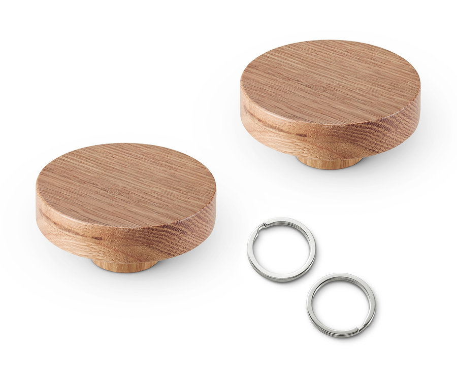 İki adet masif ahşap duvar kancası ve iki adet gümüş anahtarlık beyaz bir zemin üzerinde duruyor.