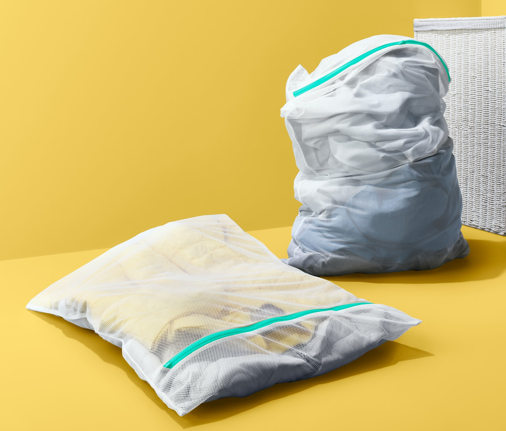 Sarı zemin üzerinde çamaşır sepetinin yanında iki adet XL çamaşır yıkama torbası duruyor.