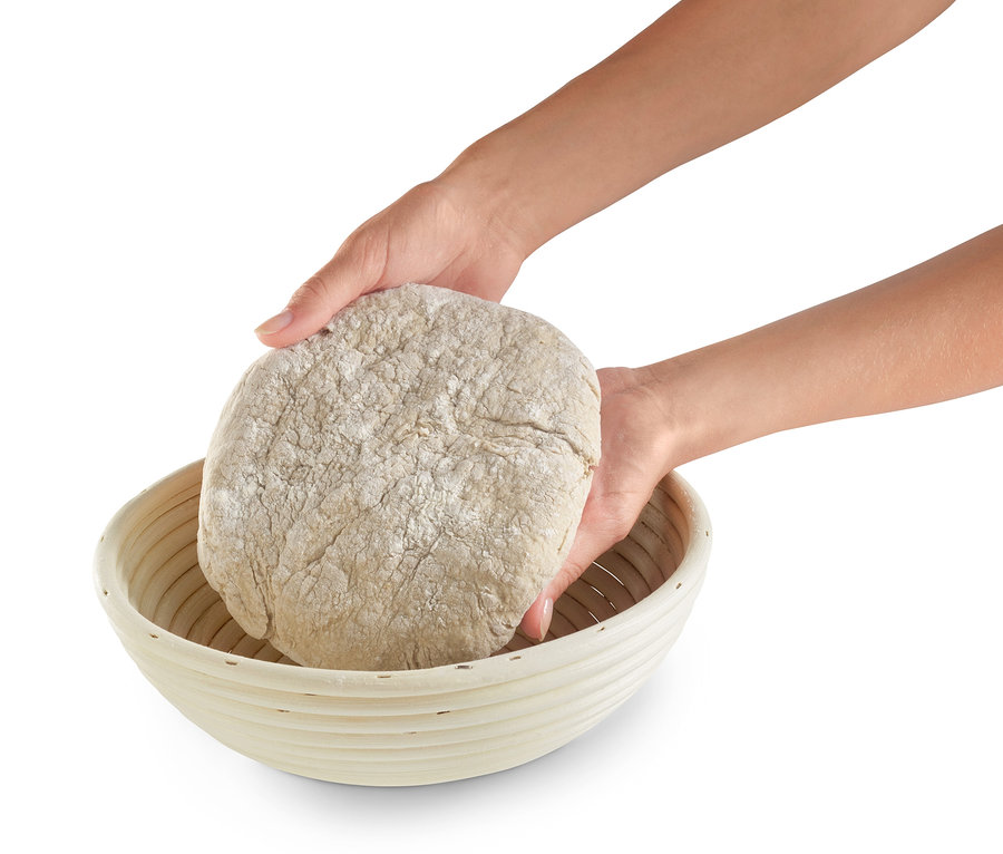 İki el bir hamur parçasını yuvarlak mayalama sepetine yerleştiriyor.