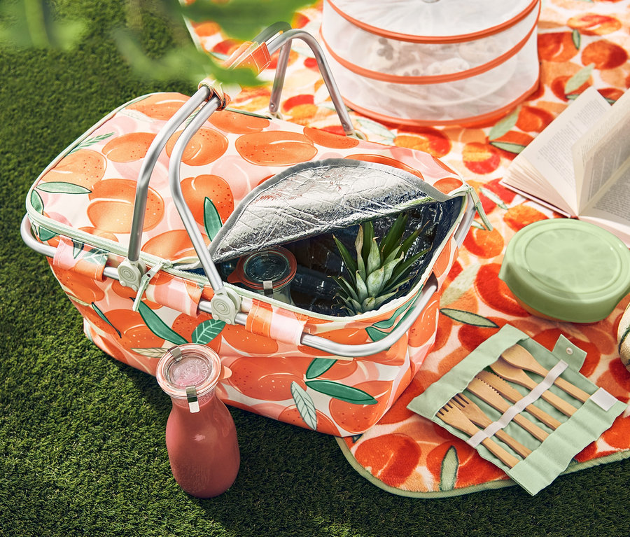 Çimenlerin üzerinde şeftali desenli XL piknik örtüsü var. Örtü üzerinde şeftali desenli soğutucu sepet, piknik çatal bıçak takımı ve katlanabilen koruyucu kapak bulunuyor.