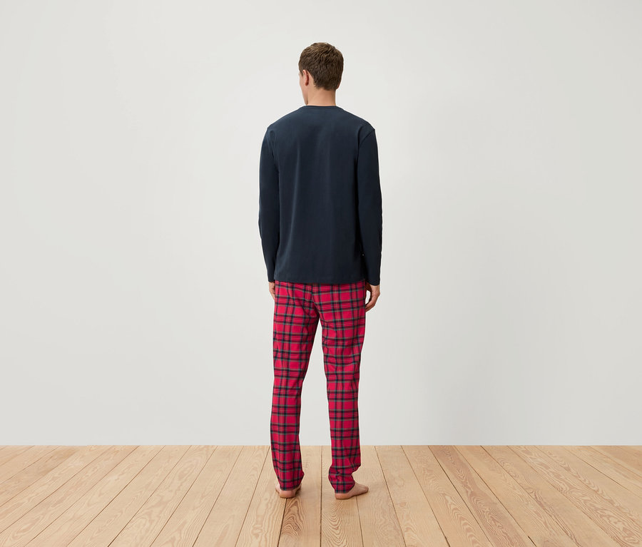 Arkası dönük bir adam, lacivert uzun kollu bir pijama üstü ve kırmızı ekose bir pijama altı giyiyor.