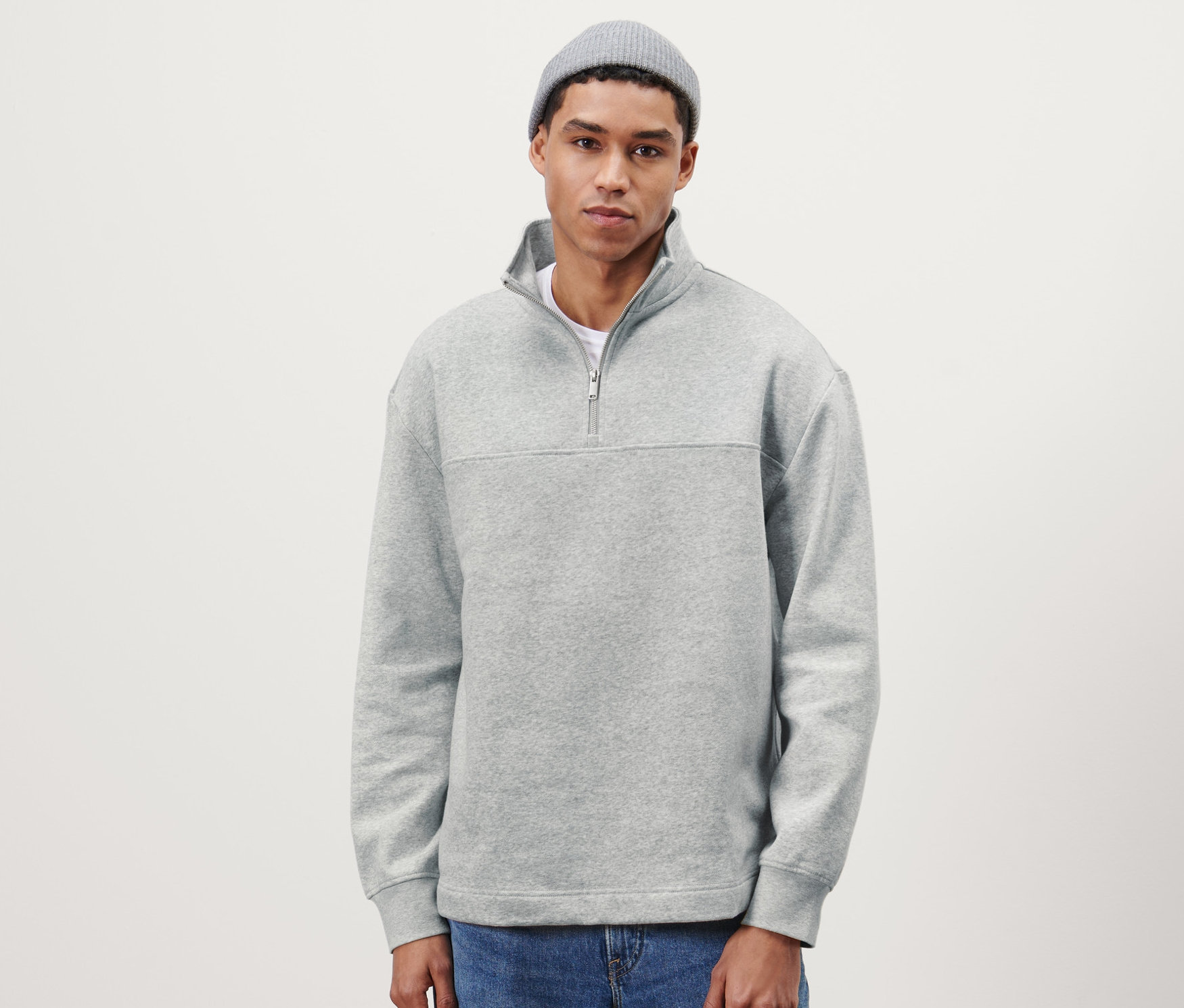 Bir adam gri Troyer kazak, kot pantolon ve gri örgü bere giyiyor.