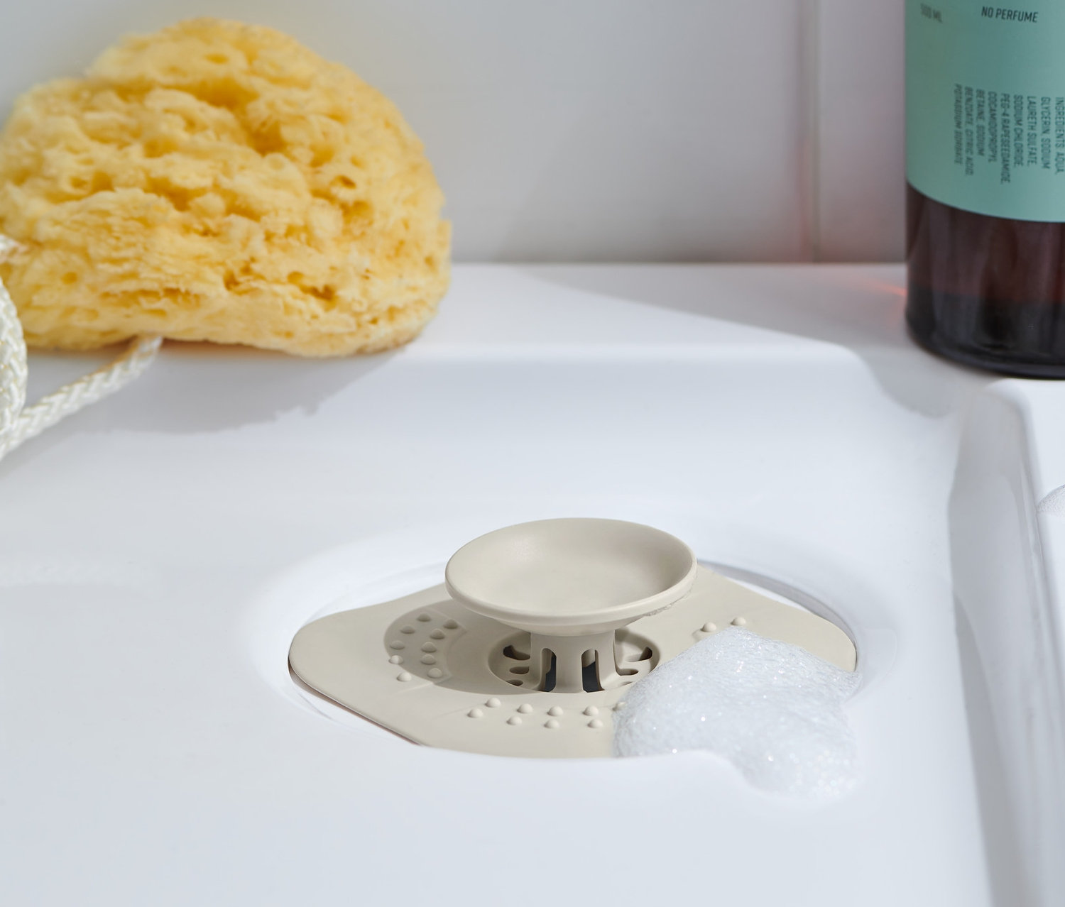 Lavaboda bir gider süzgeci/tıpa, yanında bir yıkama süngeri ve arkasında bir vücut yıkama losyonu şişesi bulunmaktadır.