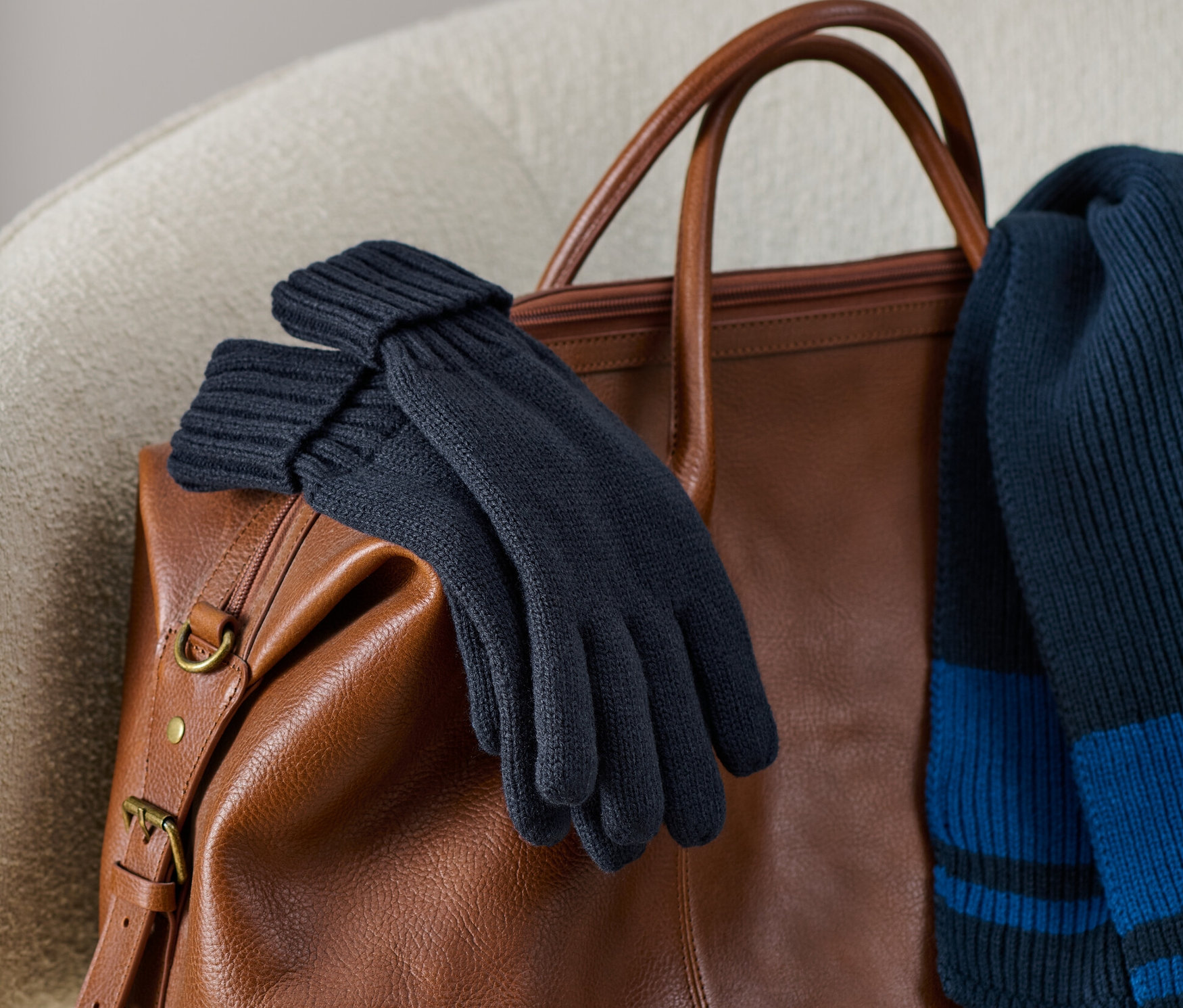 Örgü eldivenler, kahverengi deri bir çantanın üzerinde örgü bir atkıyla birlikte duruyor.