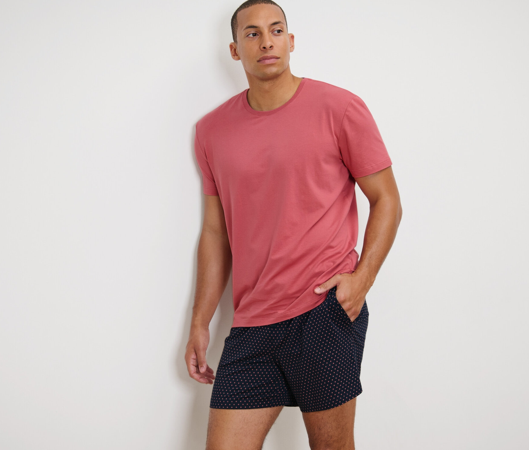 Duvara yaslanmış modal içerikli şortlu pijama takımı giyen adam.