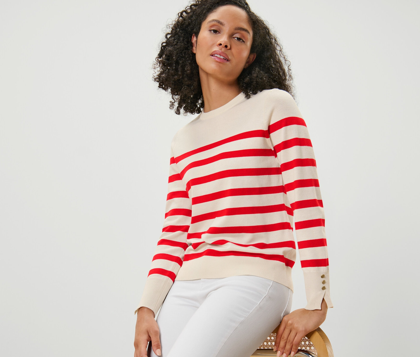 Kadın sandalyede oturuyor ve kırmızı çizgili ince örgü kazak giyiyor.