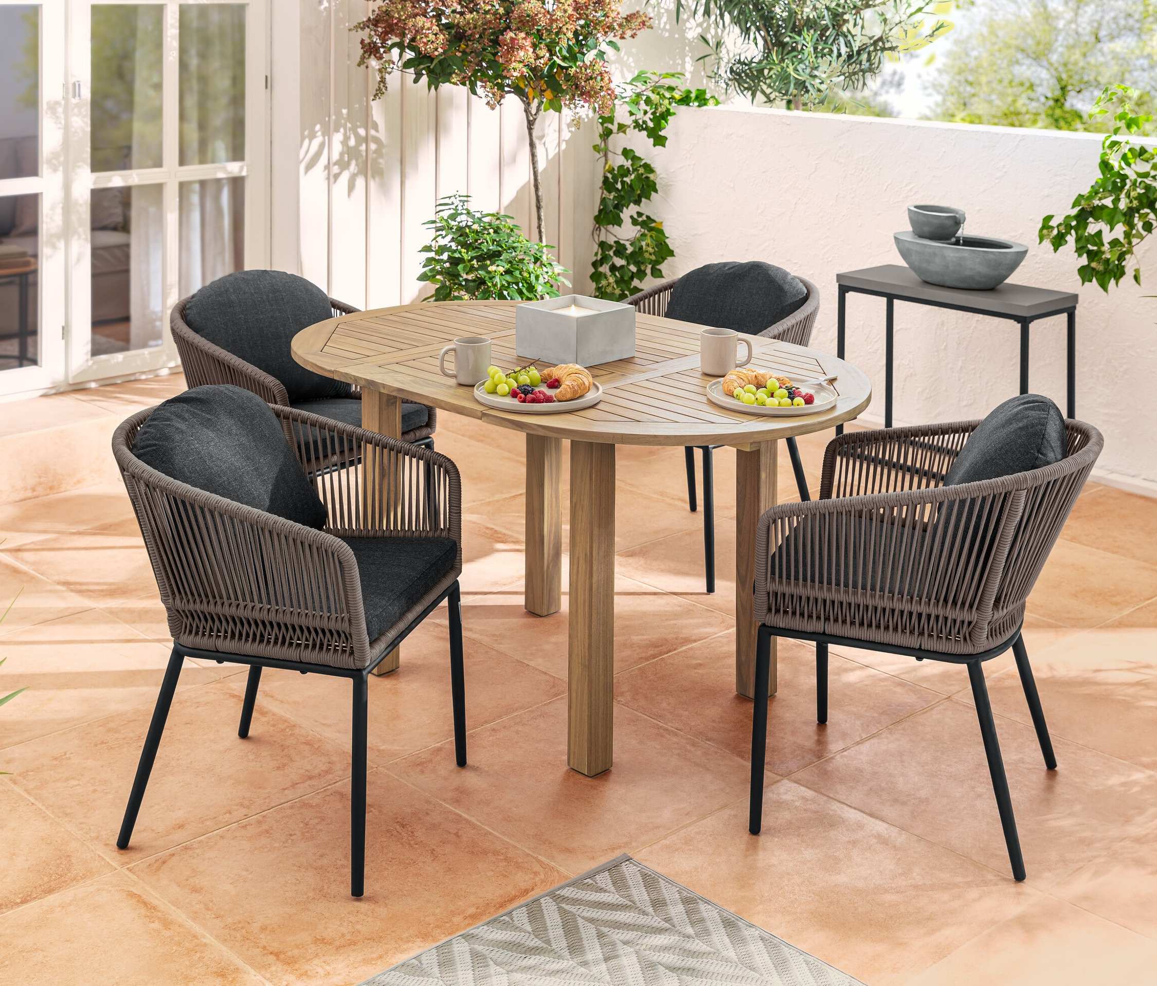 Bir terasta yemek ve içeceklerle dolu yuvarlak açılır kapanır bir masa etrafında dört adet kumaş örgülü ve yuvarlak sırtlıklı yemek sandalyesi.