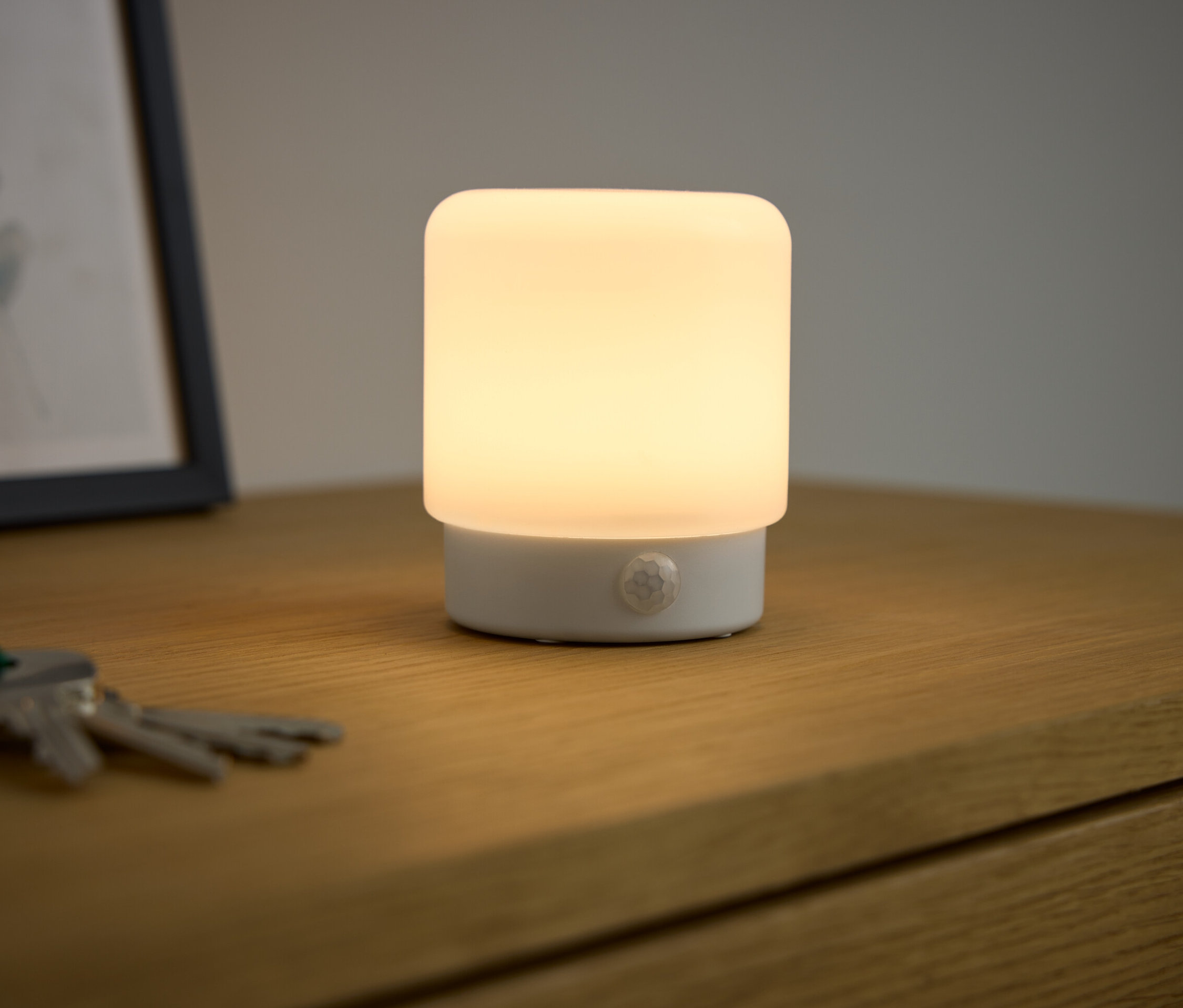 Ahşap bir masanın üzerinde LED-Mini-Multifunktionslicht mit Bewegungsmelder yanıyor ve ışık saçıyor.