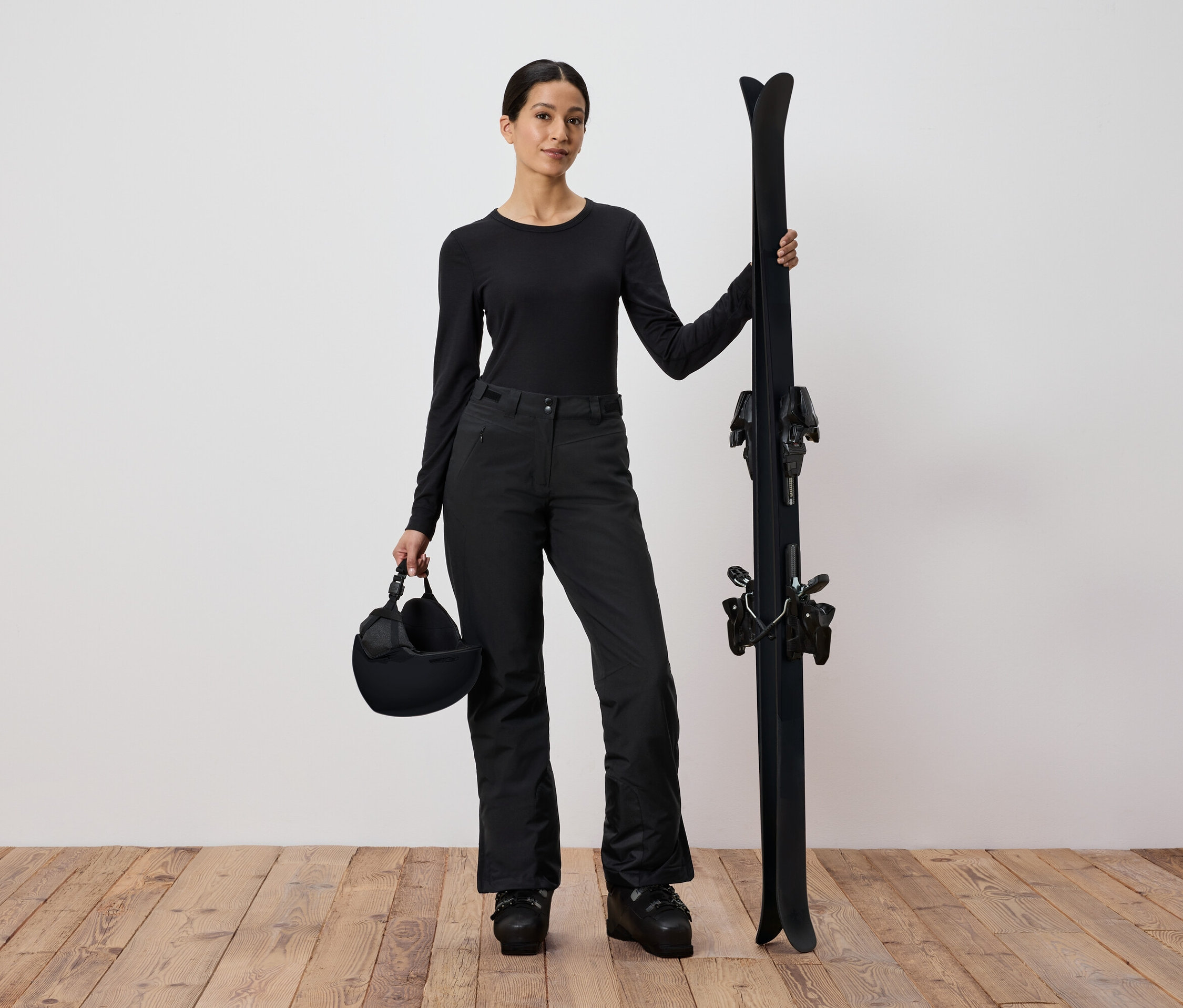Siyah kayak kıyafeti giyen kadın, kayak ve kask tutuyor.