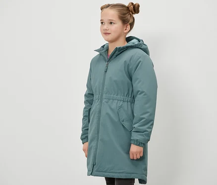 Kız çocuğu yan duruyor ve yeşil bir Kinder-Thermoparka termal parka giyiyor.