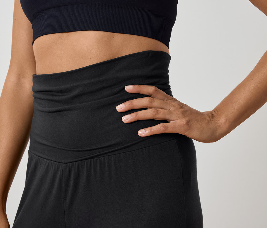 Siyah spor üstü ve yüksek belli pantolonlu bir kadın poz veriyor.