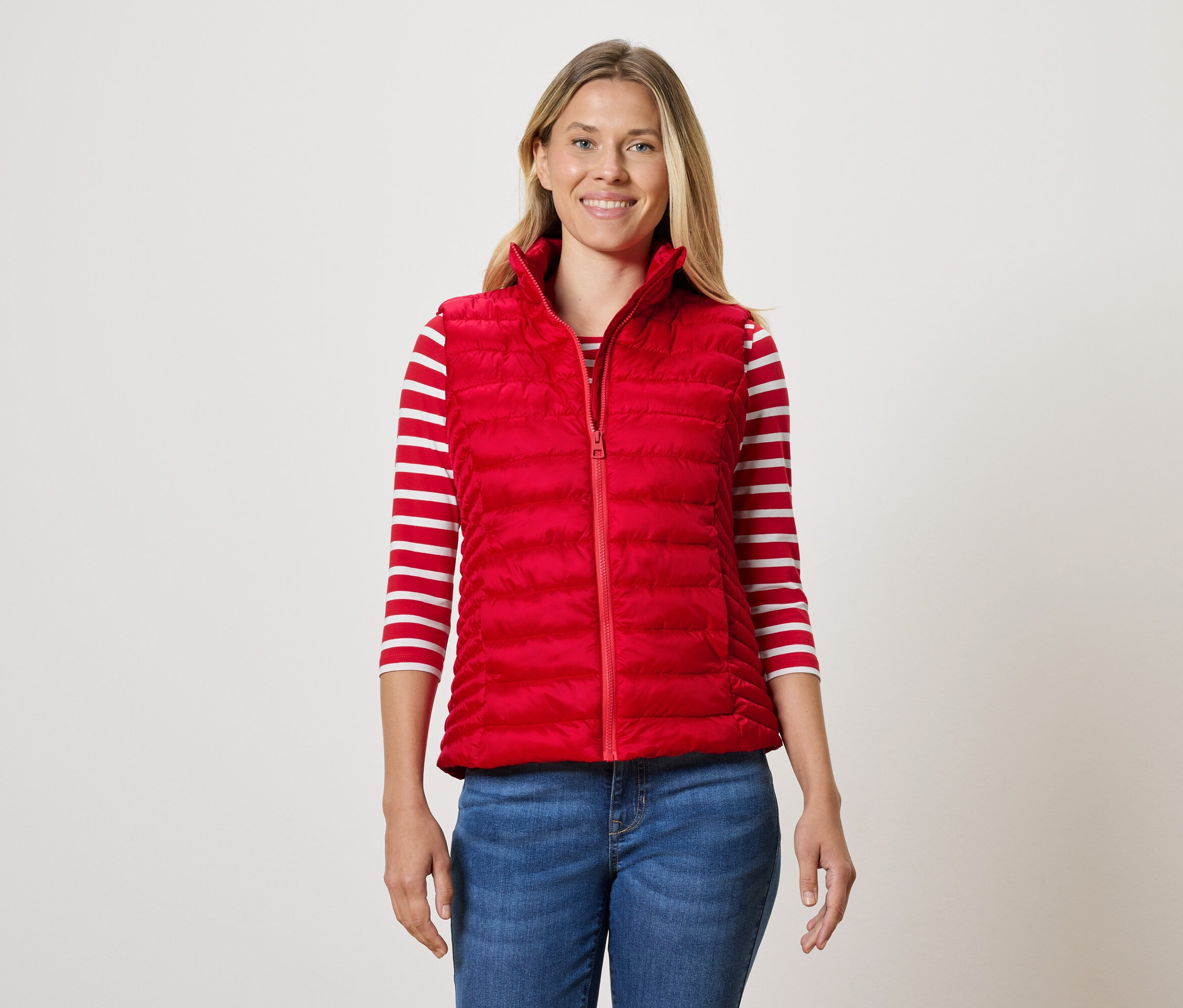 Kadın kırmızı kapitone yelek, çizgili tişört ve kot pantolon giyiyor.