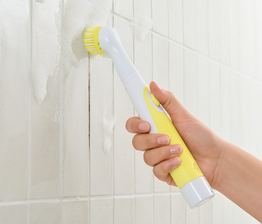 Bir el, sarı saplı elektrikli temizleme fırçası tutuyor ve beyaz fayansları temizliyor