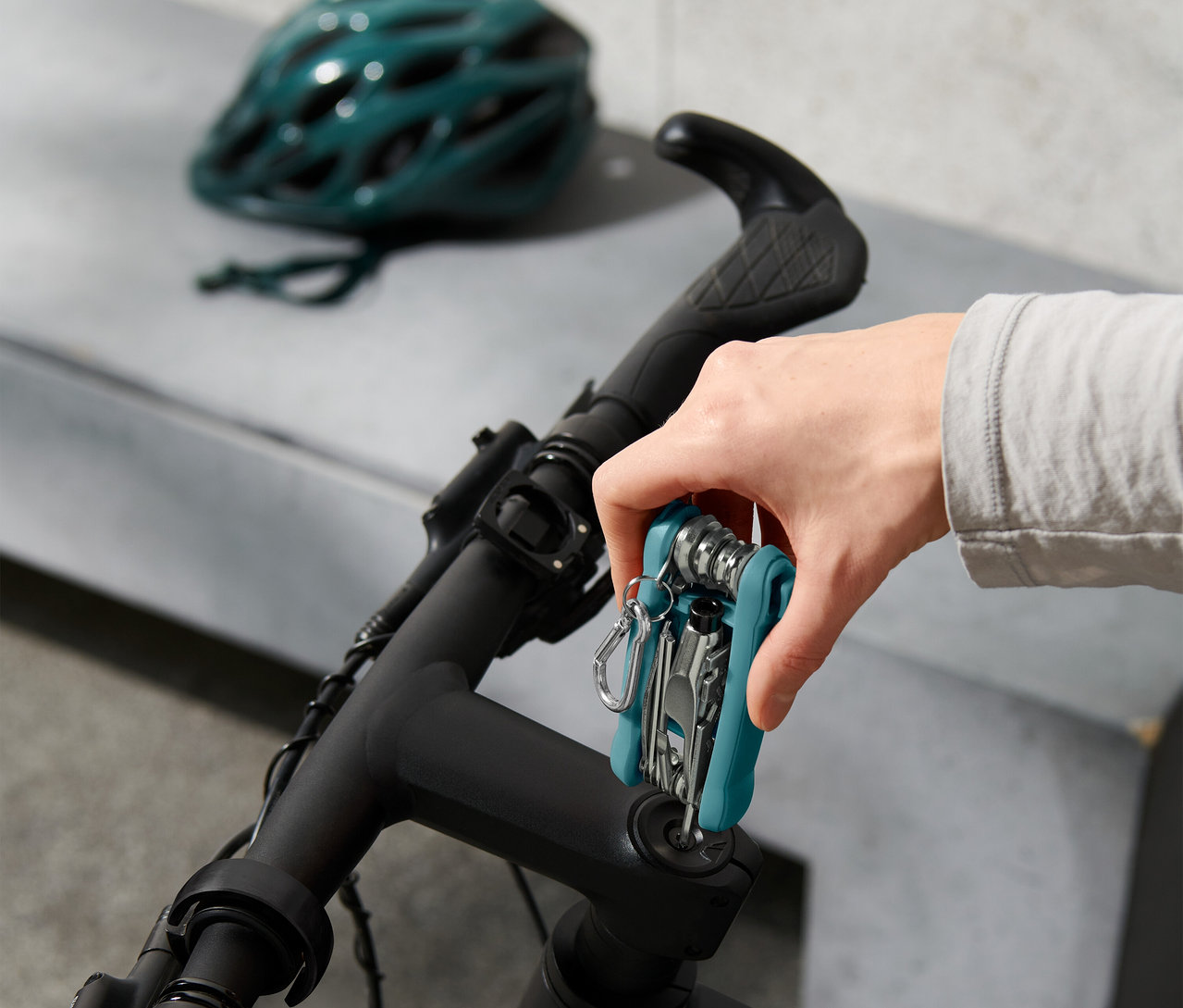 El, çok amaçlı aleti bisiklet gidonuna takıyor, arka planda bisiklet kaskı.