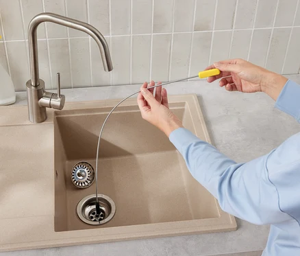 Bir kişi, mutfak lavabosu giderini temizlemek için bir lavabo açma teli kullanıyor.