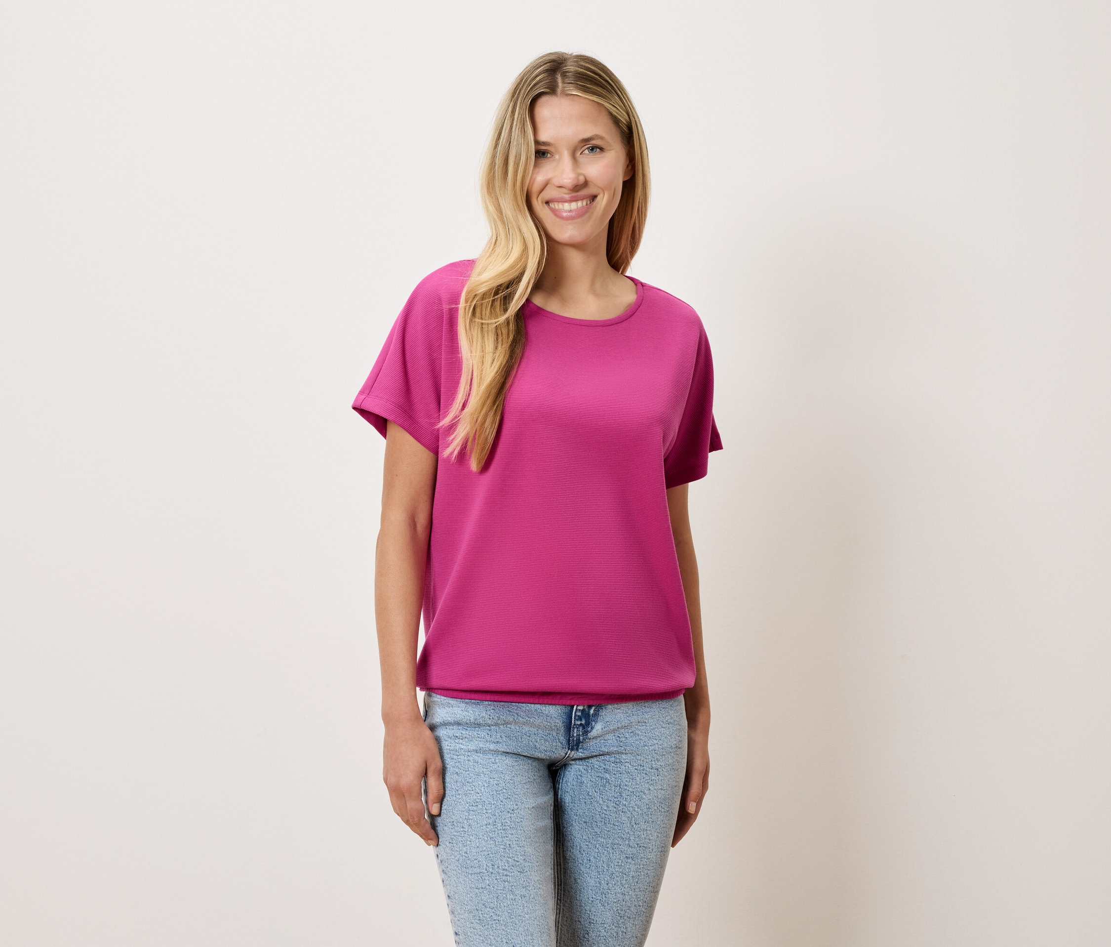 Sarışın saçlı bir kadın pembe bir tişört ve mavi kot pantolon giyiyor.