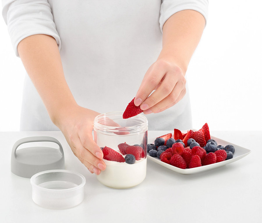 Kadın, yoğurt ve yaban mersini ile taşınabilir atıştırmalık kutusuna çilek ekliyor.