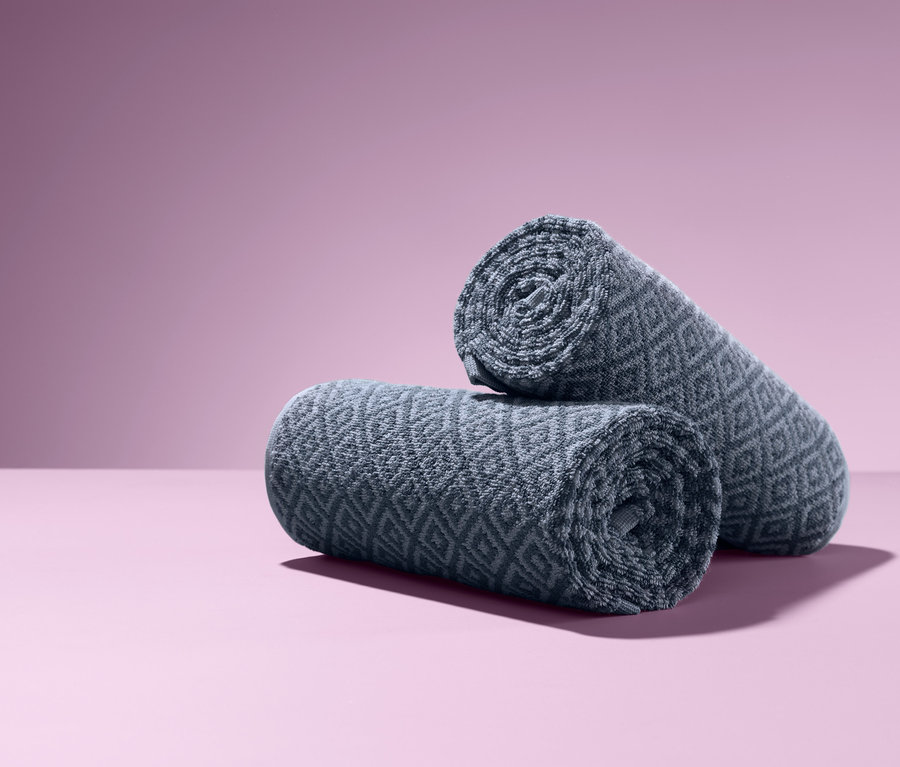 Eflatun bir arka plan üzerinde üst üste yığılmış iki adet rulo jakarlı el havlusu.