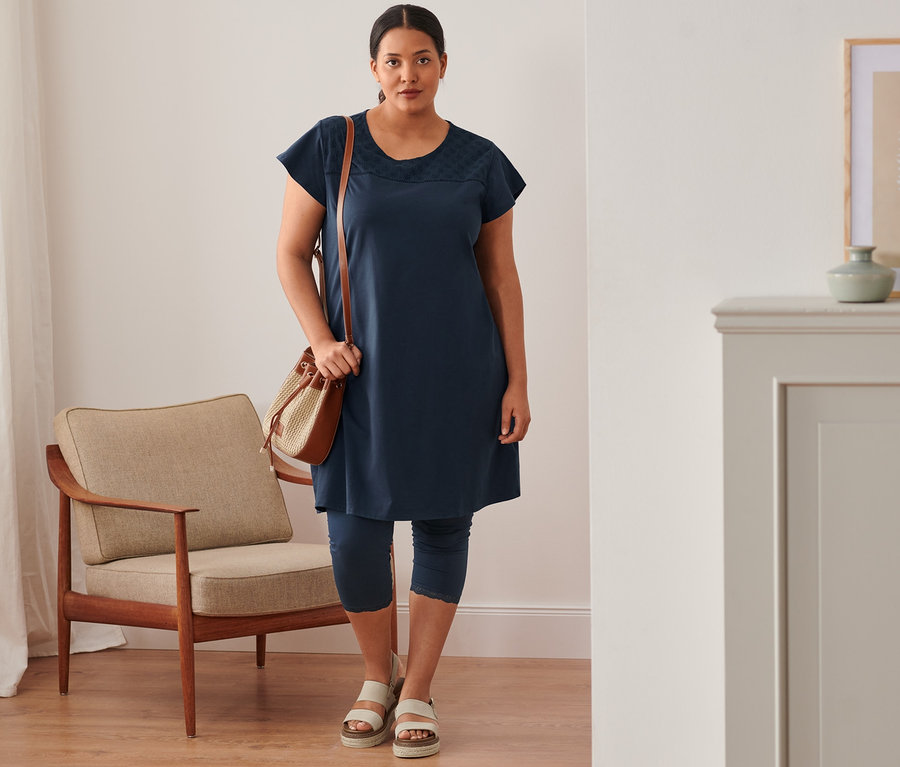 Kadın lacivert organik pamuklu kısa dantel paçalı tayt, büzgülü çanta, sandalet ve lacivert elbise giyiyor.