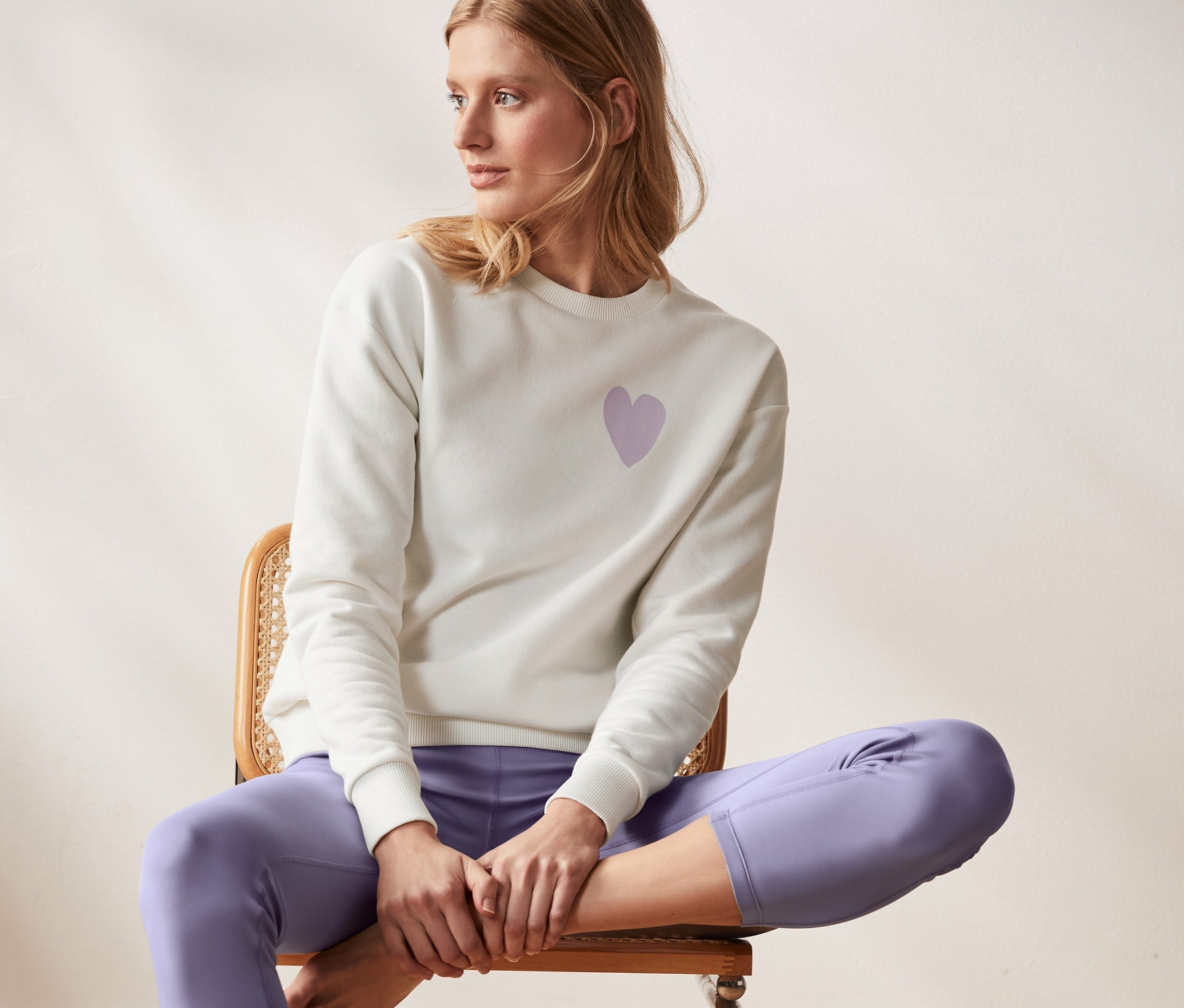 Kadın sandalyede oturuyor ve beyaz organik pamuklu sweatshirt giyiyor.