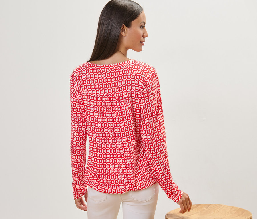 Kadın kameraya arkası dönük duruyor ve kırmızı baskılı bir bluz giyiyor.