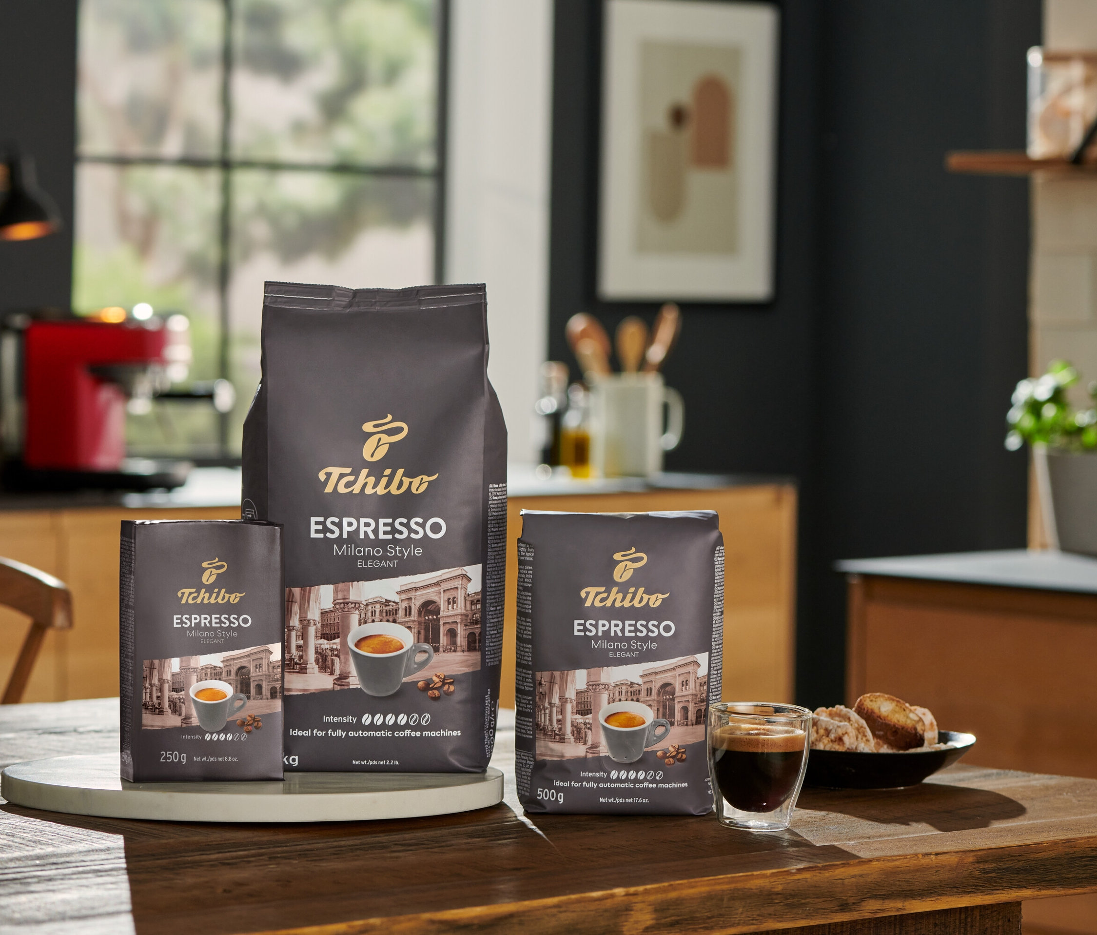 Mutfakta ahşap bir masa üzerinde üç paket Tchibo Espresso Milano Style kahve çekirdeği 250 g, 500 g ve 1 kg.