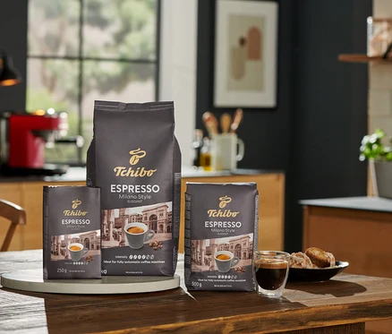 Mutfakta ahşap bir masa üzerinde üç paket Tchibo Espresso Milano Style kahve çekirdeği 250 g, 500 g ve 1 kg.