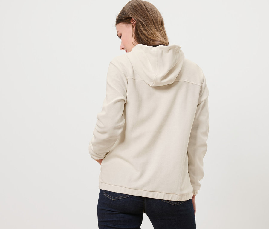Elleri cebinde krem rengi sweat mont giyen bir kadın, arkadan görünümü.