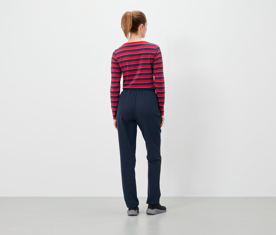 Kahverengi saçları at kuyruğu yapılmış, kırmızı-mavi çizgili uzun kollu tişört ve lacivert pantolon giyen bir kadının arka görünümü.