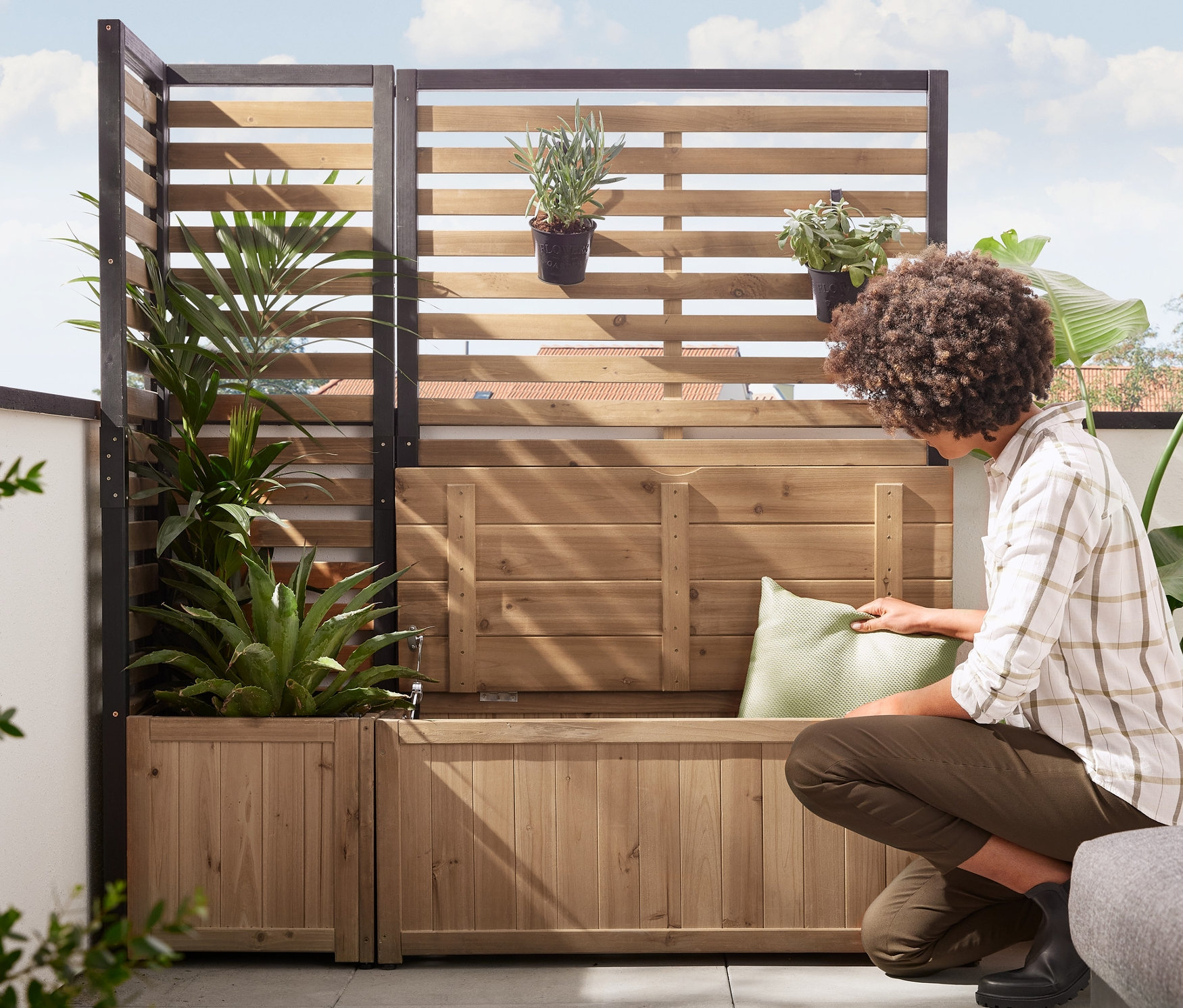 Kadın, Sandıklı Yan Paravan Modül »Elin« üzerine bir yastık yerleştiriyor. Arka planda Bitki Kasalı Korumalı Köşe Modülü »Elin« bulunuyor.