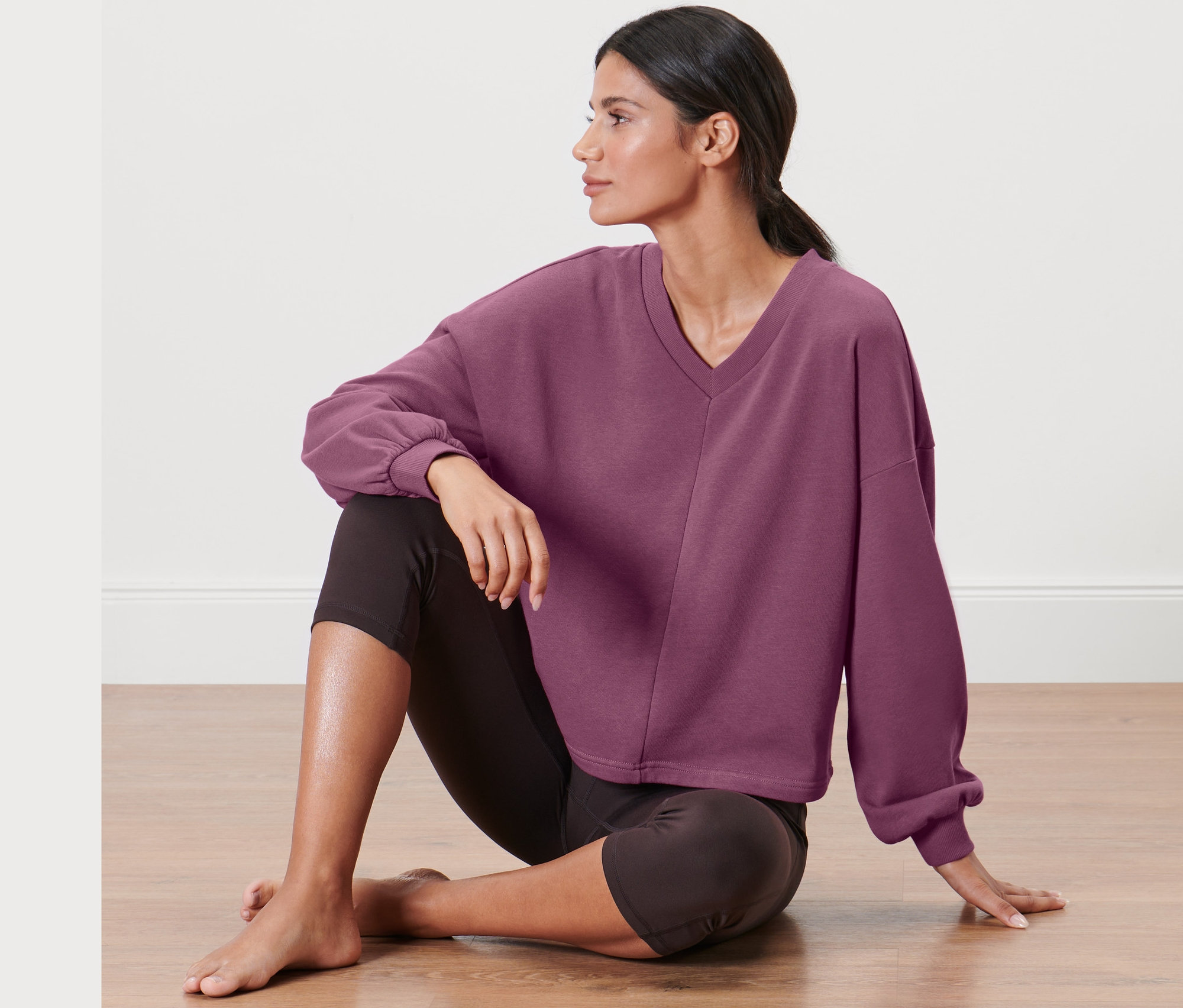 Kadın yerde oturuyor, üzerinde yoga sweatshirt var.