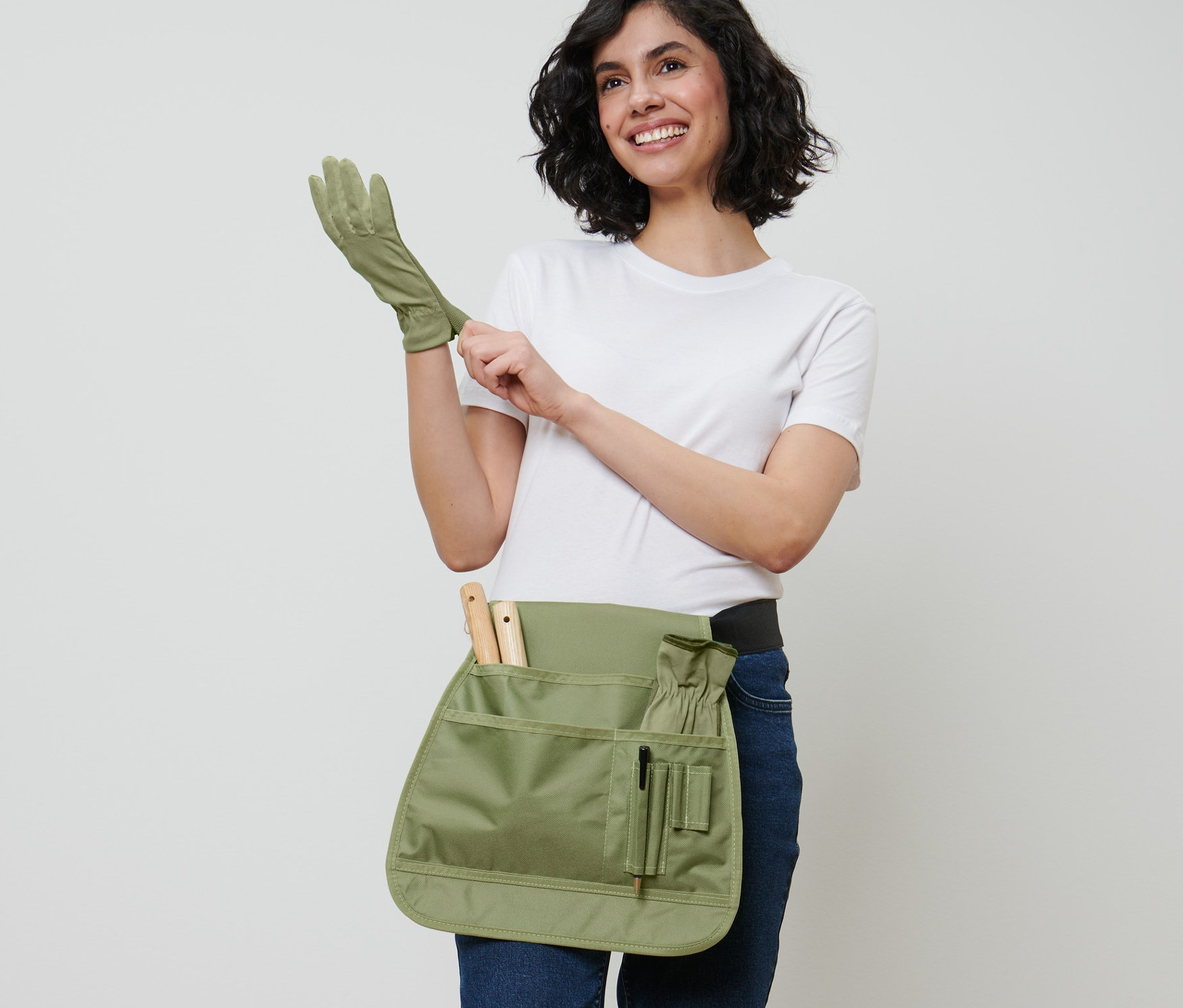 Kadın bahçıvan eldiveni giyiyor ve bir Bahçe Aletleri Kemeri takıyor.