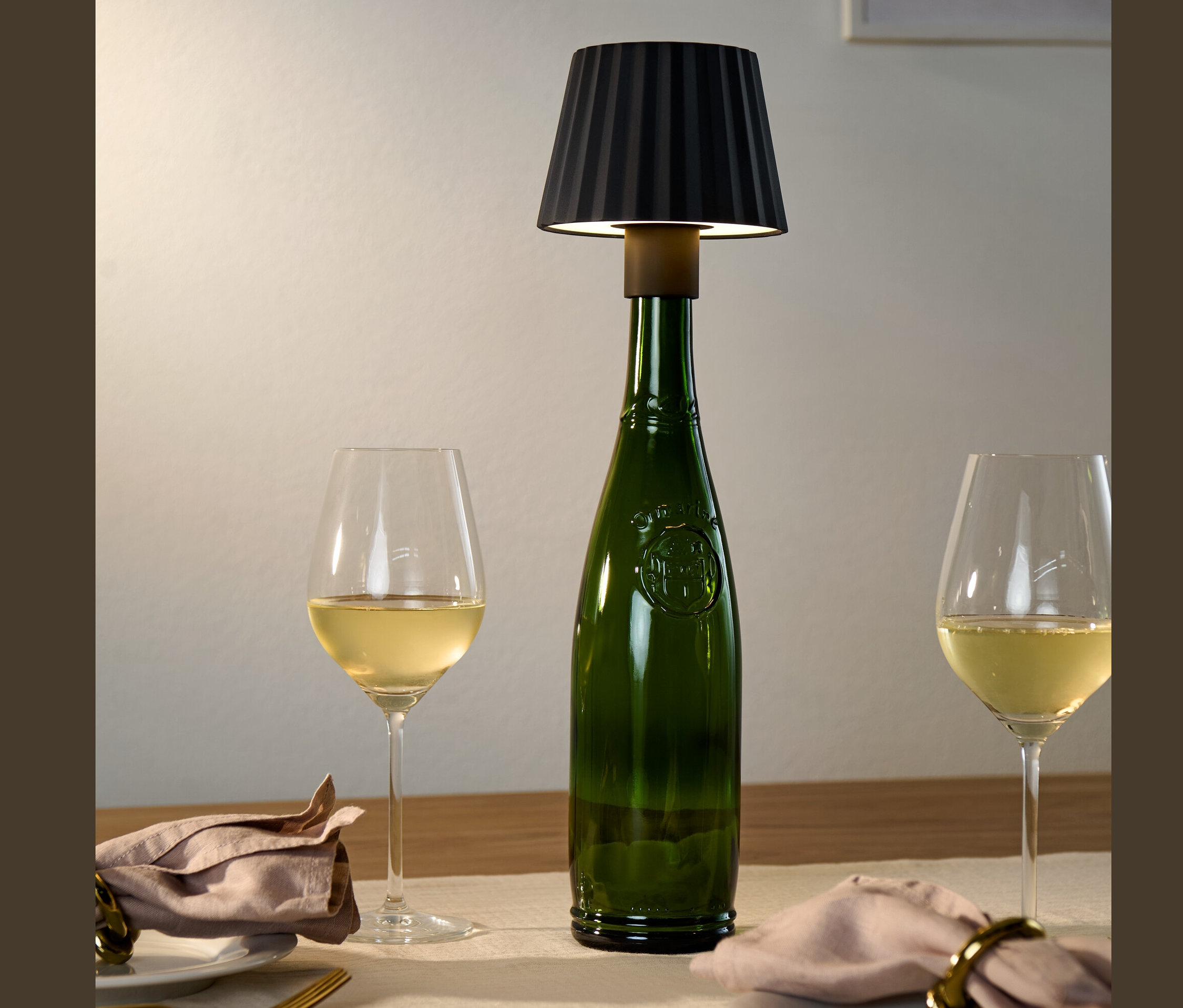 Bir masanın üzerinde siyah LED Şişe Abajur olan yeşil bir şişe ve yanında iki bardak beyaz şarap bulunmaktadır.