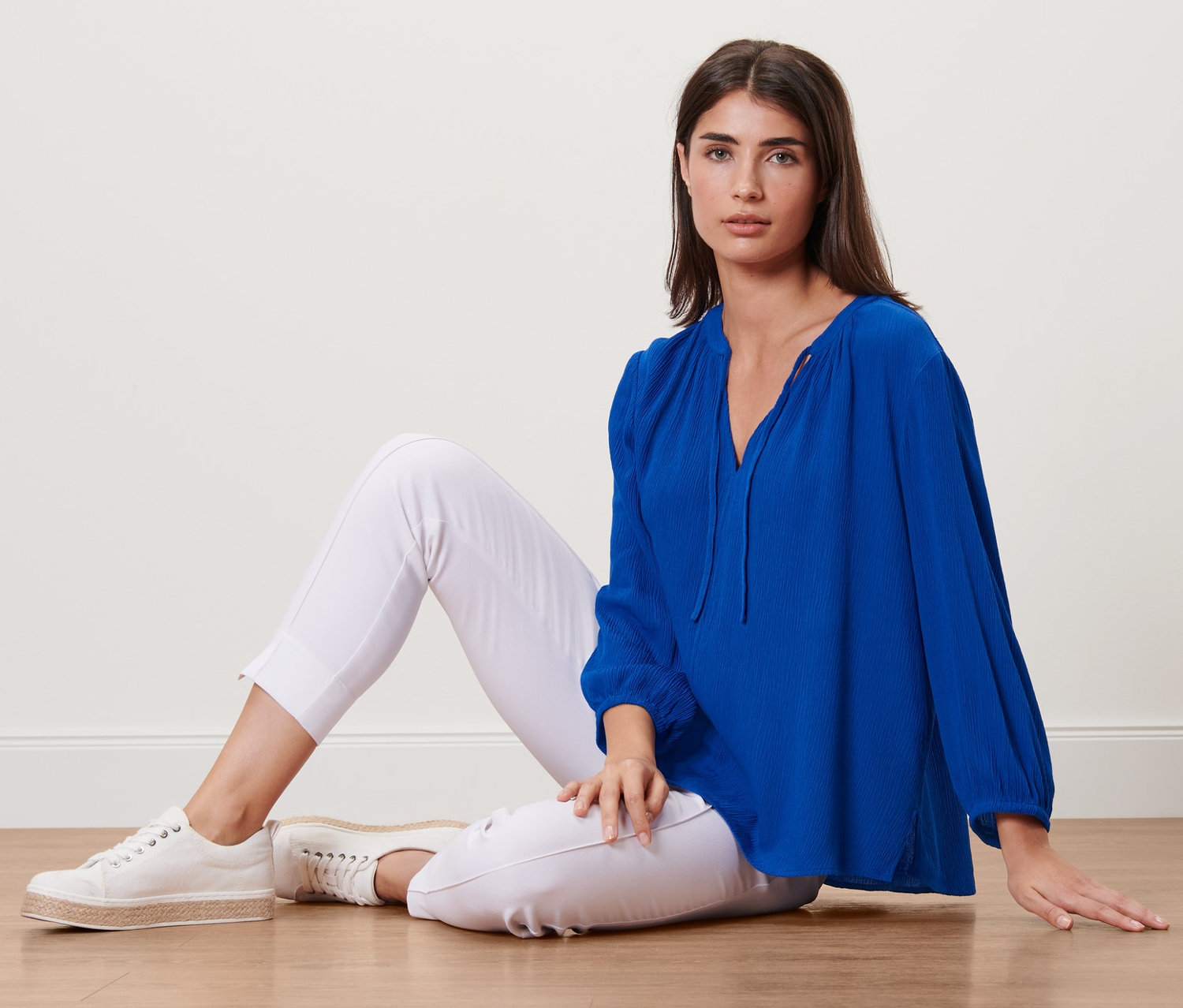 Kadın yerde oturuyor ve mavi bir tunik giyiyor.