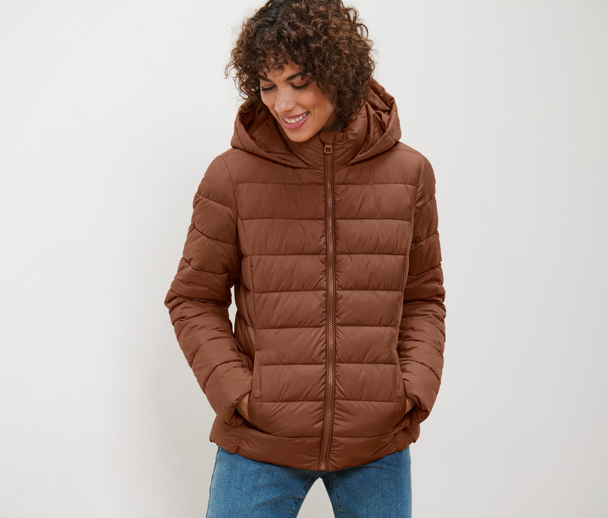 Kadın, konyak rengi kapüşonlu kapitone mont giyiyor ve aşağıya doğru bakıyor.